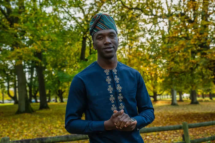 Portrait of a man in a navy embroidered outfit among autumn leaves, photographed by Imisi Bamiro, Coventry photographer