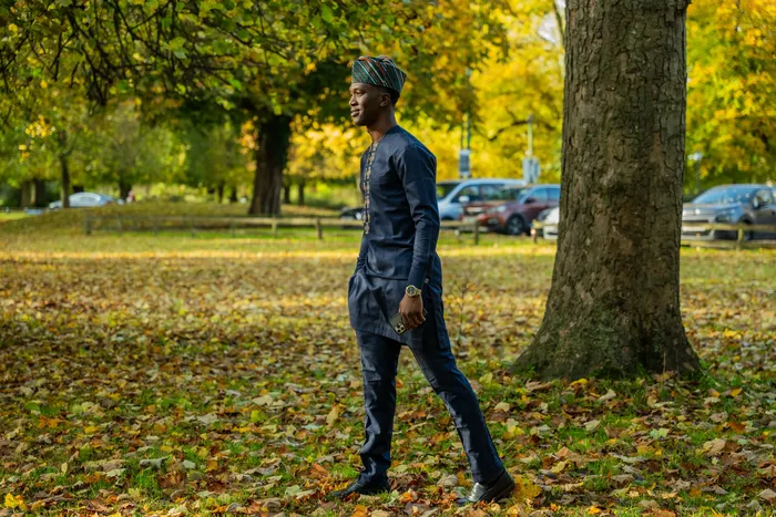 Portrait of a man in a navy embroidered outfit among autumn leaves, photographed by Imisi Bamiro, Coventry photographer