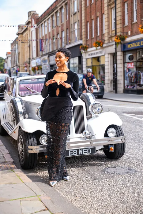 Woman in a black dress beside a vintage white car, photographed by Imisi Bamiro, Coventry photographer